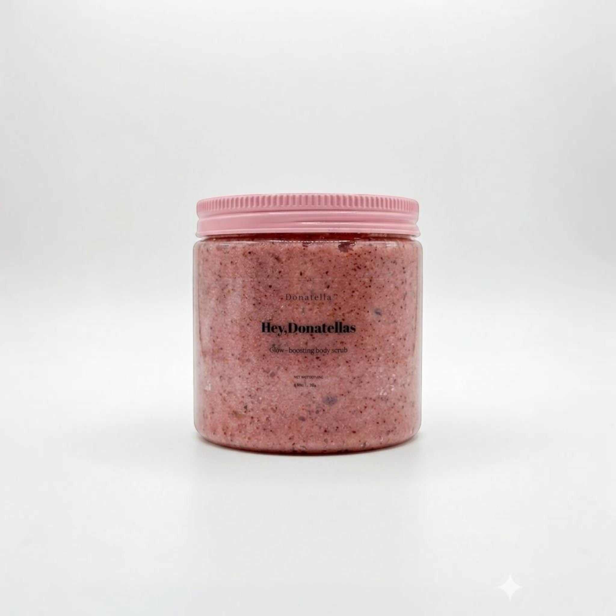 Donatella glow-boosting body scrub in a clear jar with a pink ribbed lid. The scrub is pink with visible exfoliating particles.
